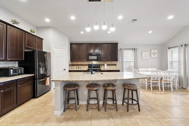 1700 Elaina Loop, Leander, TX 78641 - kitchen with black microwave, decorative backsplash, refrigerator with ice dispenser, a kitchen breakfast bar, and light stone countertops
