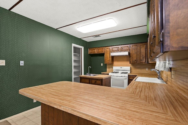 2403 N Shields Dr, Austin, TX 78727 - kitchen featuring white range with gas stovetop, under cabinet range hood, light countertops, a peninsula, and a textured ceiling