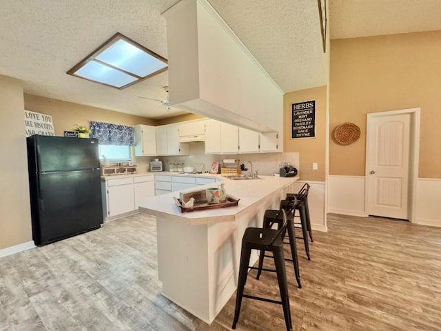 702 Pleasant Grove Rd, Elgin, TX 78621 - kitchen with freestanding refrigerator, a peninsula, light wood-style flooring, a textured ceiling, and light countertops