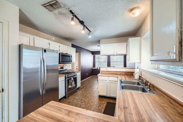 14305 Vandever St, Austin, TX 78725 - kitchen featuring stainless steel appliances, wallpapered walls, white cabinets, a textured ceiling, and a peninsula