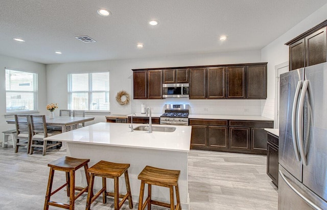 261 Deserti Rd, Leander, TX 78641 - kitchen featuring stainless steel appliances, recessed lighting, dark brown cabinetry, a kitchen bar, and light wood finished floors