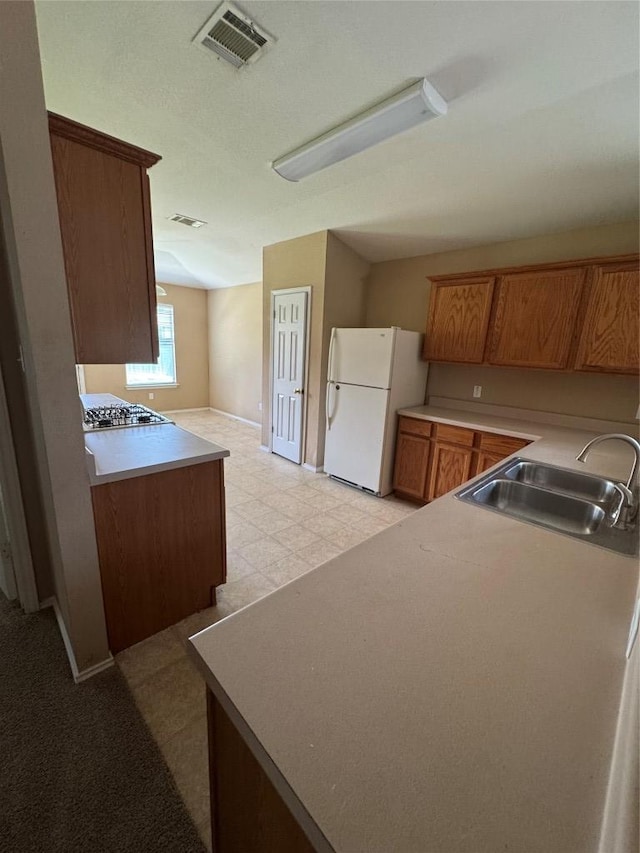 209 Lake Washington Dr, Kyle, TX 78640 - kitchen with freestanding refrigerator, stainless steel gas stovetop, light flooring, brown cabinetry, and light countertops