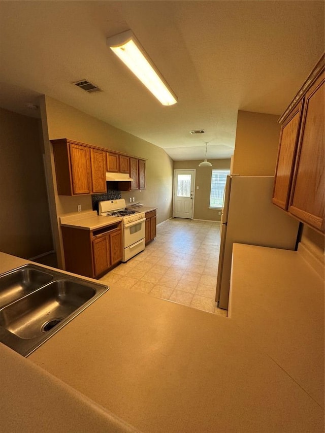 209 Lake Washington Dr, Kyle, TX 78640 - kitchen with white appliances, brown cabinets, under cabinet range hood, light countertops, and decorative light fixtures