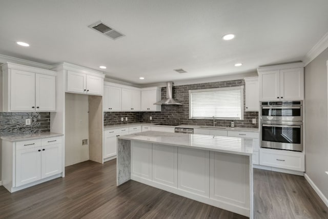 2801 Adelen Ln, Round Rock, TX 78664 - kitchen with wall chimney range hood, appliances with stainless steel finishes, tasteful backsplash, white cabinetry, and a center island