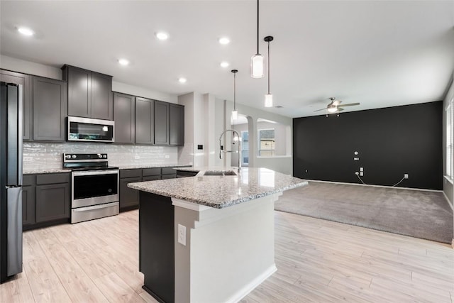101 Crimson Ln, Kyle, TX 78640 - kitchen featuring appliances with stainless steel finishes, a center island with sink, a ceiling fan, tasteful backsplash, and light stone counters