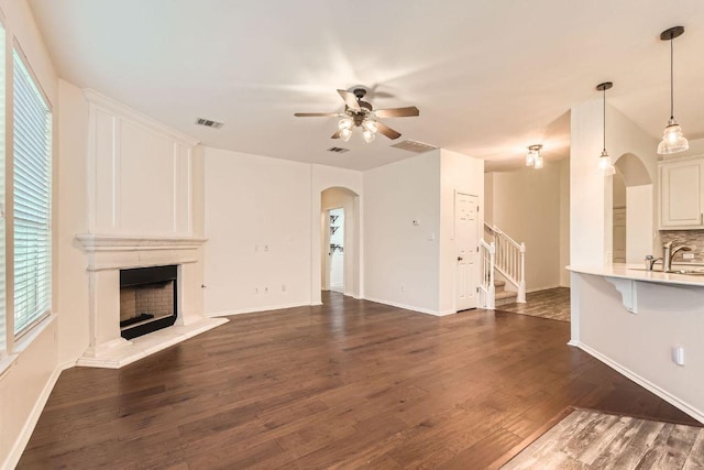 65 White Magnolia Cir, Lakeway, TX 78734 - unfurnished living room with arched walkways, ceiling fan, stairs, dark wood finished floors, and a premium fireplace