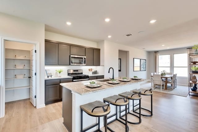 6500 Smarty Jones Ln, Buda, TX 78610 - kitchen featuring stainless steel appliances, light wood-type flooring, an island with sink, a breakfast bar, and recessed lighting