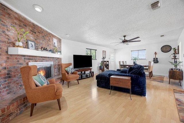 706 Cambridge Dr, Round Rock, TX 78664 - living room with light wood-style flooring, a textured ceiling, a ceiling fan, and a brick fireplace