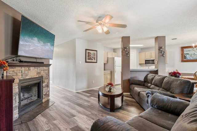 2101 Barnett Dr, Cedar Park, TX 78613 - living room featuring a textured ceiling, light wood finished floors, a ceiling fan, and a stone fireplace