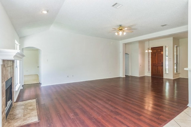 800 Mountain Ridge Dr, Leander, TX 78641 - unfurnished living room with arched walkways, ceiling fan, a tiled fireplace, wood finished floors, and vaulted ceiling