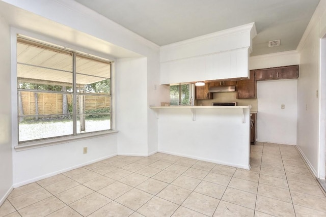 803 Easy Day Cv, Austin, TX 78745 - kitchen featuring under cabinet range hood, crown molding, light countertops, light tile patterned floors, and a peninsula