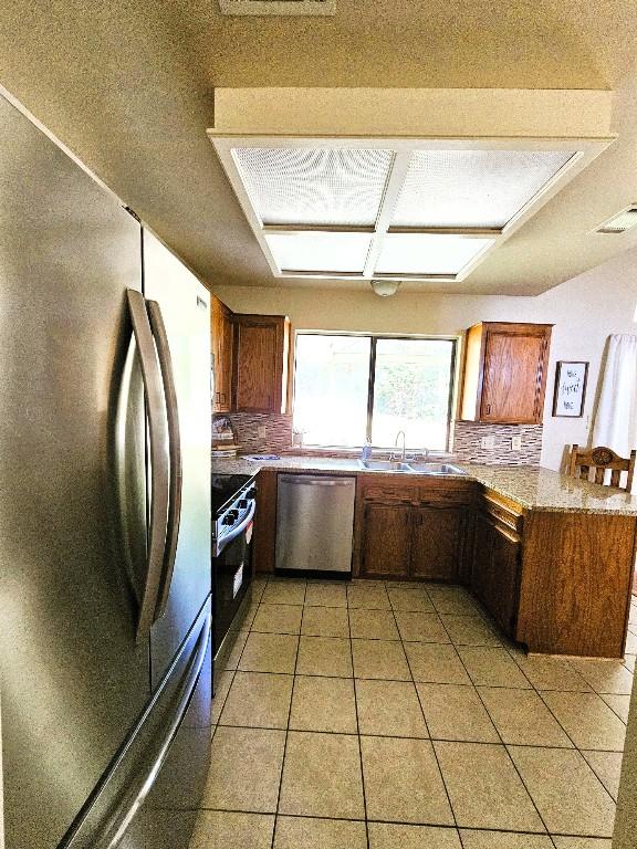 1202 Bowen Ave, Copperas Cove, TX 76522 - kitchen featuring appliances with stainless steel finishes, a peninsula, light tile patterned floors, brown cabinets, and light countertops