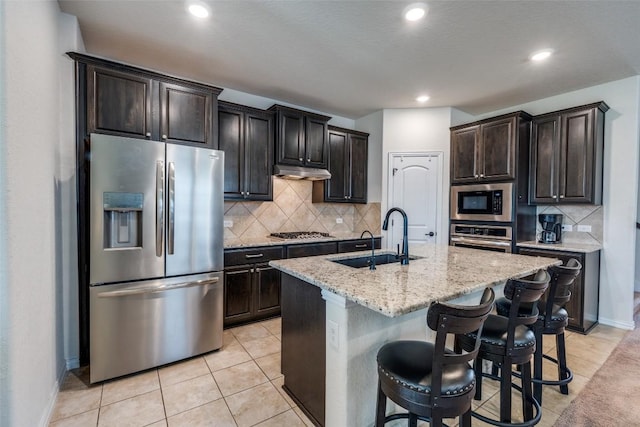1624 Stone House Dr, New Braunfels, TX 78132 - kitchen with stainless steel appliances, backsplash, a center island with sink, light stone countertops, and under cabinet range hood