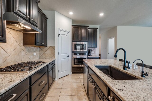 1624 Stone House Dr, New Braunfels, TX 78132 - kitchen with appliances with stainless steel finishes, under cabinet range hood, decorative backsplash, light stone countertops, and recessed lighting