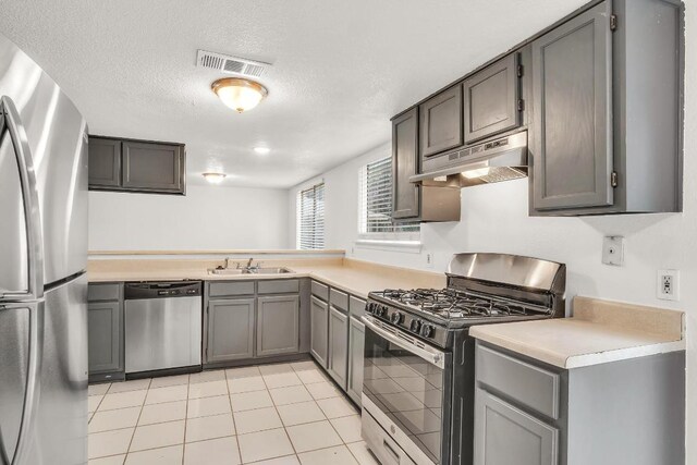 9611 Meadowheath Dr, Austin, TX 78729 - kitchen with appliances with stainless steel finishes, under cabinet range hood, gray cabinetry, light countertops, and a textured ceiling