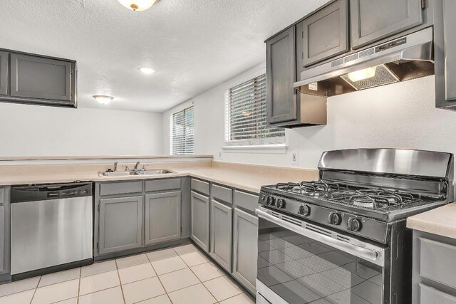 9611 Meadowheath Dr, Austin, TX 78729 - kitchen featuring appliances with stainless steel finishes, under cabinet range hood, a textured ceiling, gray cabinetry, and light countertops