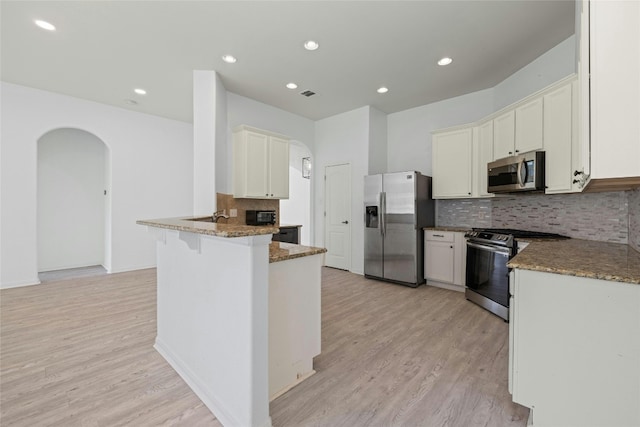 4204 Pasada Ln, Round Rock, TX 78681 - kitchen featuring stainless steel appliances, arched walkways, dark stone counters, light wood-type flooring, and a peninsula