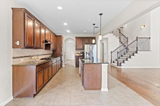 112 Florenz Ln, Georgetown, TX 78628 - kitchen featuring arched walkways, appliances with stainless steel finishes, dark stone countertops, under cabinet range hood, and decorative backsplash