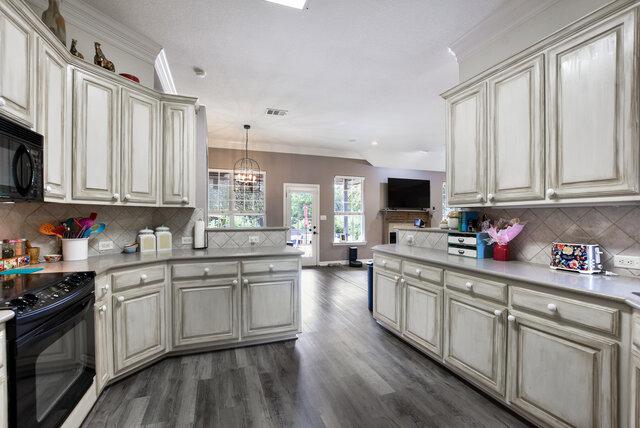 1906 W Moeta Dr, Austin, TX 78734 - kitchen featuring black appliances, dark wood-type flooring, a peninsula, light countertops, and decorative backsplash