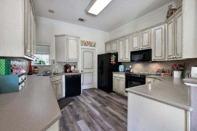 1906 W Moeta Dr, Austin, TX 78734 - kitchen with black appliances, ornamental molding, cream cabinets, decorative backsplash, and wood finished floors