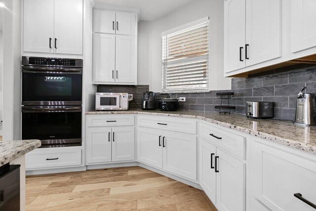 110 Les Ln, Smithville, TX 78957 - kitchen with stainless steel double oven, white microwave, white cabinets, tasteful backsplash, and light wood-style floors