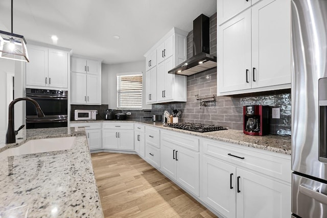 110 Les Ln, Smithville, TX 78957 - kitchen with wall chimney range hood, appliances with stainless steel finishes, white cabinets, decorative backsplash, and light wood-type flooring