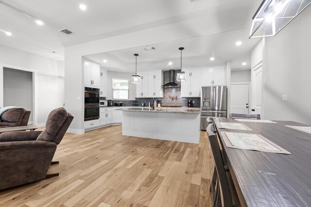 110 Les Ln, Smithville, TX 78957 - kitchen with wall chimney exhaust hood, appliances with stainless steel finishes, open floor plan, light wood-type flooring, and decorative backsplash