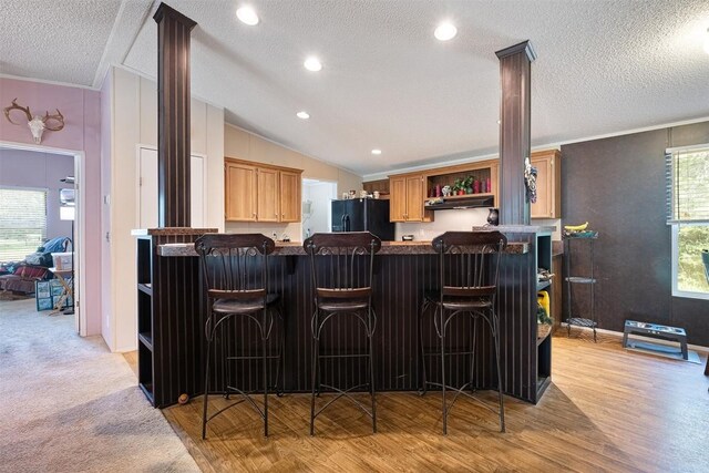 1231 Peach Creek Rd, Waelder, TX 78959 - indoor bar with black fridge with ice dispenser, under cabinet range hood, crown molding, vaulted ceiling, and light wood-type flooring