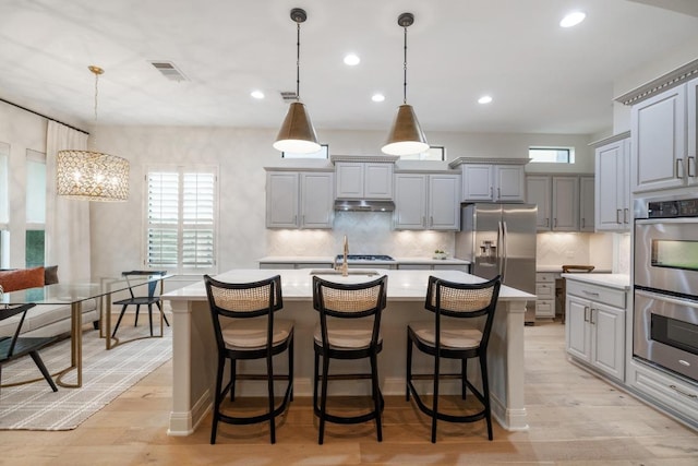 114 Reflection Bay Ct, Austin, TX 78738 - kitchen featuring gray cabinetry, appliances with stainless steel finishes, under cabinet range hood, light countertops, and a center island with sink