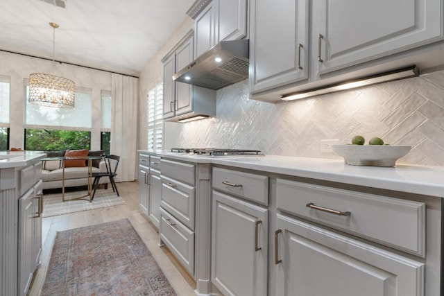 114 Reflection Bay Ct, Austin, TX 78738 - kitchen with exhaust hood, gray cabinetry, stainless steel gas cooktop, and decorative backsplash