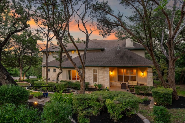 7709 Waldon Dr, Austin, TX 78750 - back of property at dusk featuring stone siding, an outdoor hangout area, a shingled roof, a patio, and stucco siding