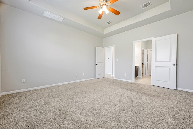 1017 Sundrops St, Leander, TX 78641 - unfurnished bedroom with a tray ceiling, light carpet, connected bathroom, and a ceiling fan