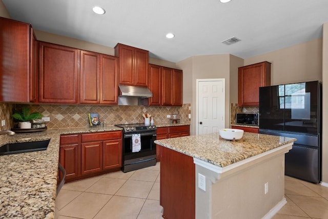 1012 Autumn Sage Way, Pflugerville, TX 78660 - kitchen with appliances with stainless steel finishes, under cabinet range hood, light tile patterned flooring, light stone counters, and a kitchen island