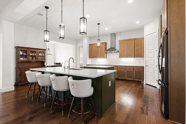 104 Huerta Rd, Florence, TX 76527 - kitchen featuring wall chimney range hood, a kitchen island with sink, freestanding refrigerator, dark wood-style floors, and light countertops