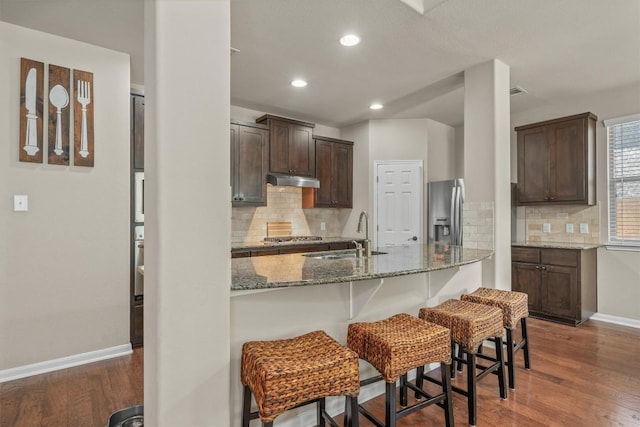 204 Archipelago Trl, Austin, TX 78717 - kitchen with appliances with stainless steel finishes, a breakfast bar area, dark brown cabinets, light stone countertops, and wood finished floors