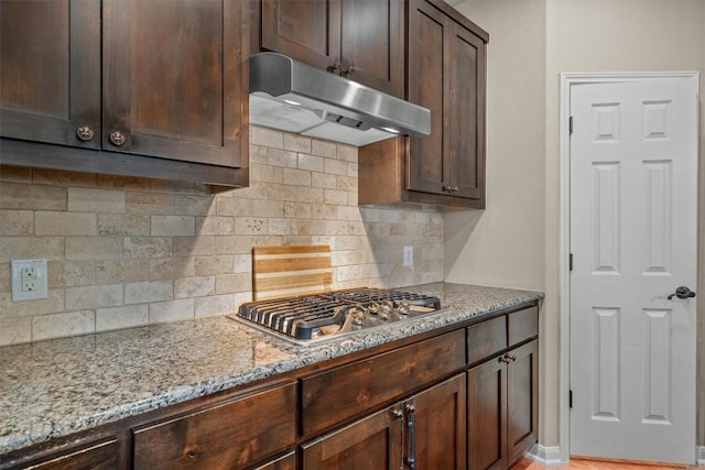 204 Archipelago Trl, Austin, TX 78717 - kitchen featuring under cabinet range hood, stainless steel gas stovetop, light stone counters, dark brown cabinetry, and tasteful backsplash