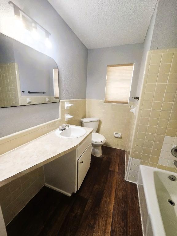 917 Edwards St S, Copperas Cove, TX 76522 - full bathroom featuring tile walls, wood finished floors, a bathtub, a textured ceiling, and vanity