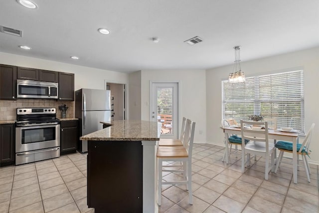 509 Red Tailed Hawk Dr, Pflugerville, TX 78660 - kitchen featuring stainless steel appliances, light tile patterned floors, a kitchen island, tasteful backsplash, and a kitchen bar