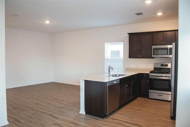 13801 Tordillo Dr, Elgin, TX 78621 - kitchen featuring appliances with stainless steel finishes, wood finished floors, a peninsula, dark brown cabinetry, and light countertops