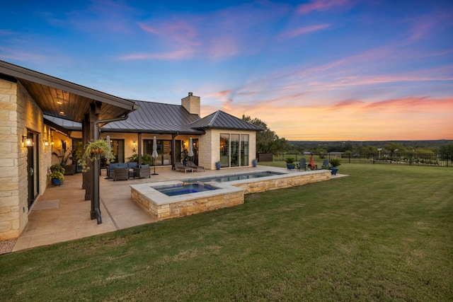 196 Westgate Loop, Horseshoe Bay, TX 78657 - back of property at dusk featuring a standing seam roof, a chimney, a patio, an in-ground hot tub, and outdoor lounge area