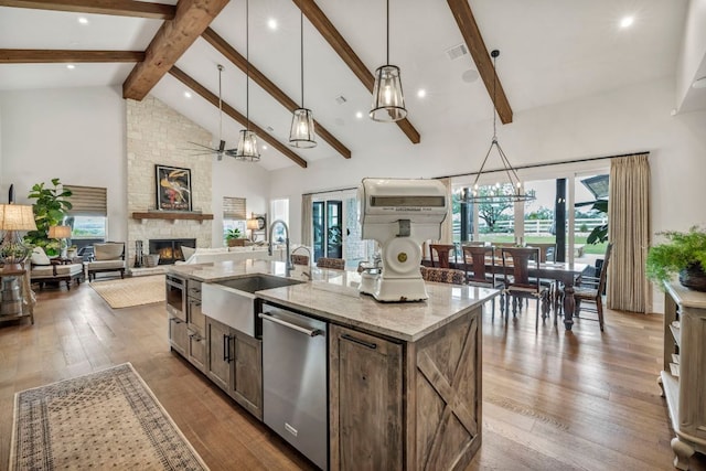 196 Westgate Loop, Horseshoe Bay, TX 78657 - kitchen featuring dishwasher, a stone fireplace, an island with sink, light stone countertops, and beam ceiling