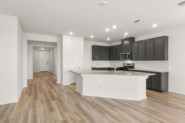 3715 Liberi Ln, Round Rock, TX 78665 - kitchen featuring appliances with stainless steel finishes, tasteful backsplash, light wood-style flooring, a kitchen island with sink, and recessed lighting