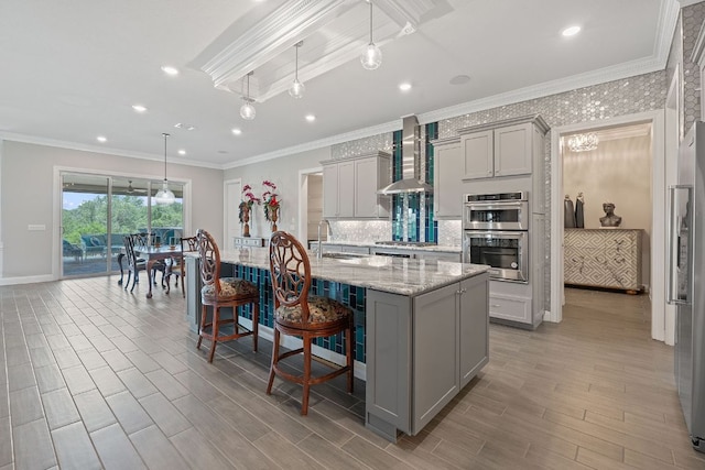 306 Iron Rail Ln, Georgetown, TX 78633 - kitchen with gray cabinets, wall chimney range hood, stainless steel appliances, a kitchen breakfast bar, and light wood-style floors
