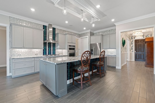 306 Iron Rail Ln, Georgetown, TX 78633 - kitchen featuring wall chimney range hood, gray cabinets, appliances with stainless steel finishes, a kitchen island with sink, and backsplash