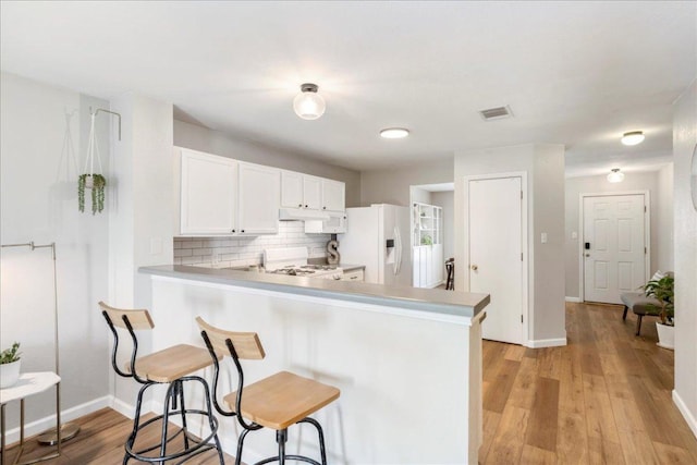 161 Buttercup Way, Kyle, TX 78640 - kitchen with white refrigerator with ice dispenser, a breakfast bar, under cabinet range hood, decorative backsplash, and white cabinets