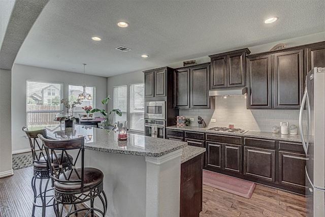 536 Middle Brook Dr, Leander, TX 78641 - kitchen featuring stainless steel appliances, a kitchen bar, a kitchen island, light wood finished floors, and tasteful backsplash