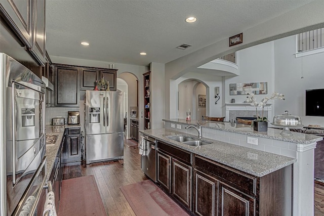 536 Middle Brook Dr, Leander, TX 78641 - kitchen with appliances with stainless steel finishes, arched walkways, a center island with sink, dark wood finished floors, and a textured ceiling