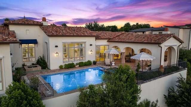4716 Peralta Ln, Austin, TX 78735 - back of house at dusk featuring a tiled roof, a chimney, an outdoor pool, stucco siding, and a patio area