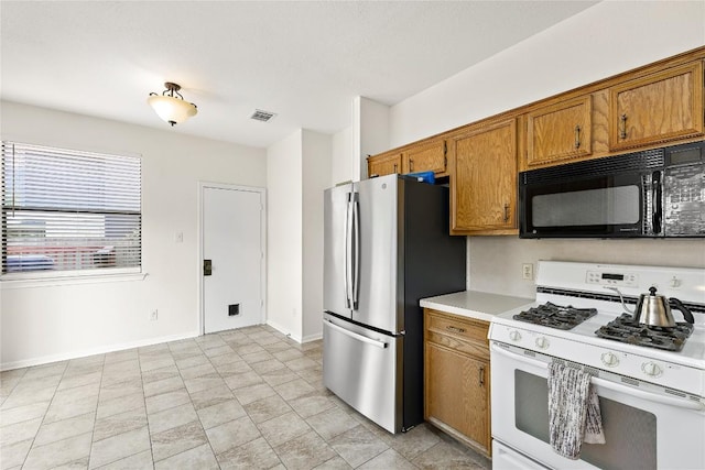 5910 Abilene Trl, Austin, TX 78749 - kitchen featuring white range with gas stovetop, black microwave, freestanding refrigerator, brown cabinets, and light countertops