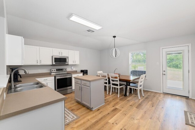 5601 Malcom Trl, Austin, TX 78754 - kitchen featuring appliances with stainless steel finishes, light wood finished floors, a kitchen island, white cabinets, and decorative light fixtures